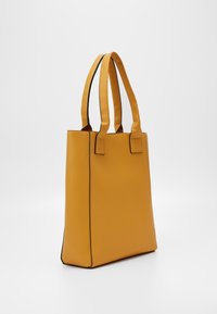 Żółta torba tote o fakturze, z dwoma prostymi uchwytami, z kontrastującym czarnym wykończeniem wzdłuż krawędzi oraz usystematyzowanym prostokątnym kształtem.