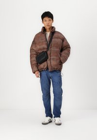 Gevoerde bruine jas met een subtiel patroon, gecombineerd met blauwe jeans en witte sneakers. Heeft ook een zwarte crossbody tas.