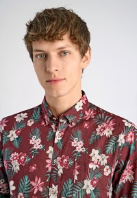 Korte mouwen bordeaux shirt met bloemen- en bladpatronen in roze, wit en teal. Voorzien van een knoopsluiting bij de kraag en een lichte textuur.