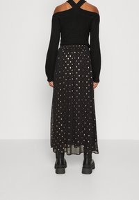 Svart lång kjol i genomskinligt tyg med ett prickigt rosaguldsmönster, kombinerad med en svart texturerad off-shoulder-tröja och kraftiga svarta stövlar.