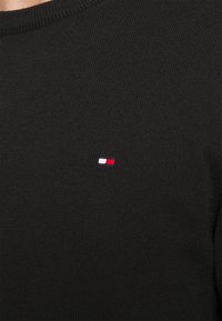 Pull en maille noire avec un petit logo brodé aux accents rouge, blanc et bleu sur le côté gauche de la poitrine. Col rond, coupe régulière.