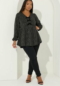 Top peplum nero con un motivo testurizzato, dotato di scollatura a V e tre accenti a fiocco neri, abbinato a pantaloni neri aderenti e tacchi a strappo.