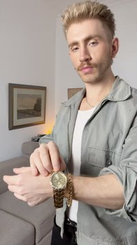 Goldene Uhr mit rundem Ziffernblatt, metallischem Gliederarmband und drei kleinen Zifferblättern. Trägt man an einem Handgelenk mit einer goldenen Kettenarmband.