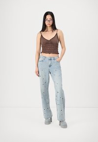 Brun ruchet crop topp med tynne stropper, kombinert med lyseblå denimjeans med sirkulære utskjæringer og en avslappet straight-leg design.