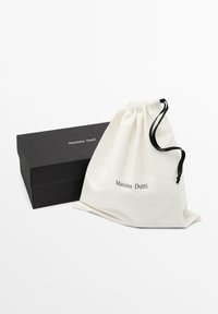 Woreczny plecak z materiału w kolorze kremowym z czarnym sznurkiem, z logo "Massimo Dutti". W zestawie z czarnym kartonowym pudełkiem o prostym wzorze.