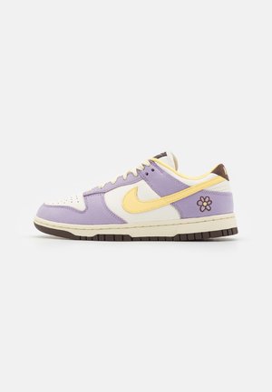 Lage sneaker met lavendel- en crèmekleurige panelen, gele Nike-swoosh, bruine zool en geborduurde bruine en gele bloem op de hiel.