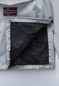 Grå jakke med et norsk flag patch. Har en lynlåselomme med sort mesh-for og glat overflade.