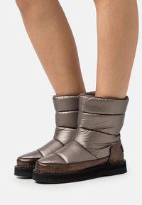 Metallisch graue Knöchelstiefel mit gepolstertem Design, runder Zehenform, kontrastierender dunkler Sohle und dezenten Nähdetails.