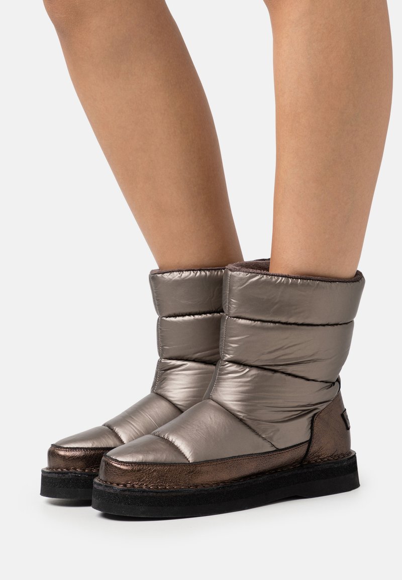 Metallisch graue Knöchelstiefel mit gepolstertem Design, runder Zehenform, kontrastierender dunkler Sohle und dezenten Nähdetails.