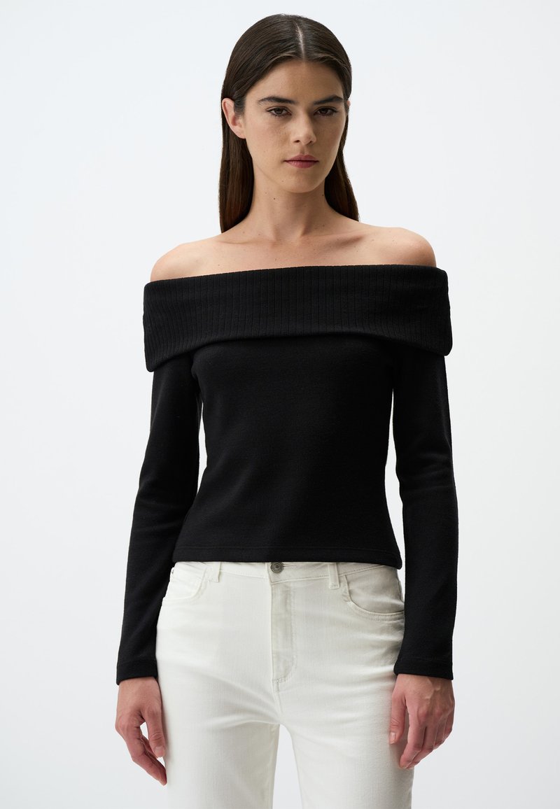 Zwarte off-the-shoulder top gemaakt van ribbenstof, slim fit lange mouwen, gestructureerde halslijn, gecombineerd met witte jeans en minimale hardware.