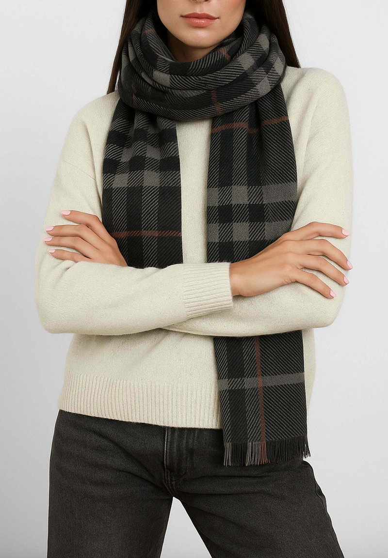 Sciarpa a quadri nera e grigia realizzata in tessuto morbido, con estremità a frange e una linea accentuata arancione, avvolta attorno a un maglione neutro.