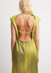 Back view of a sleeveless, green dress with a deep V-cut, features a smooth, shiny texture and button detail at the neck.