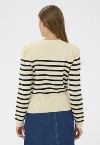 Pull rayé crème et marine, avec un ourlet côtelé, une silhouette ajustée et des manches bouffantes. Textile doux avec des couleurs contrastées.