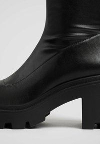 Bottines noires en cuir avec une finition lisse, semelle en caoutchouc épaisse et talon bloc angulaire. Caractéristiques d'un design minimaliste avec des accents texturés.