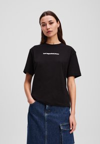 T-shirt en coton noir à manches courtes, avec un texte blanc qui indique "karl lagerfeld jeans" sur la poitrine. Design simple, coupe décontractée.