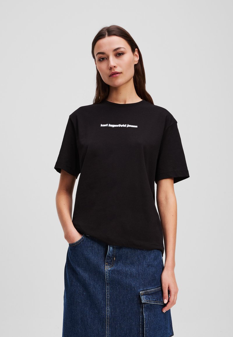 T-shirt en coton noir à manches courtes, avec un texte blanc qui indique "karl lagerfeld jeans" sur la poitrine. Design simple, coupe décontractée.
