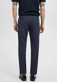 Pantalons de costume bleu marine avec une coupe ajustée, dotés de deux poches arrière et d'une texture lisse, assortis à des chaussures de ville noires.