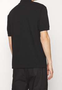Polo noir à manches courtes avec un col classique, fabriqué en tissu lisse, présentant une coupe droite sans logos ni motifs visibles.