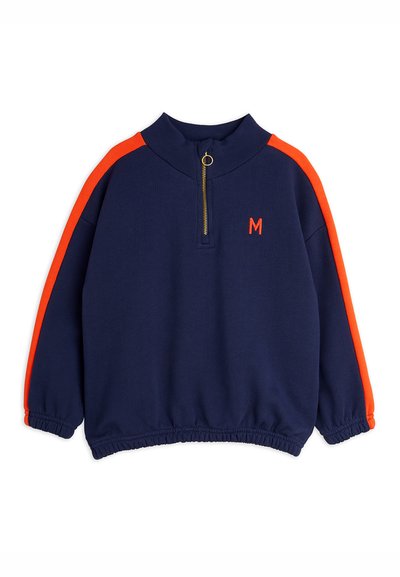 Temno modra športna majica z visokim ovratnikom, pol zadrgo, oranžnimi poudarnimi črtami na ramenih in vezenim logotipom "M" v oranžni barvi.