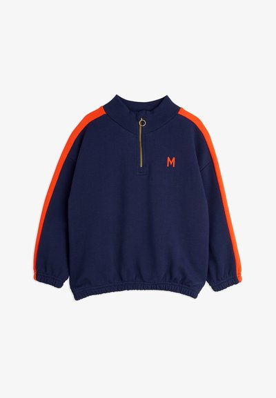 Temno modra športna majica z visokim ovratnikom, pol zadrgo, oranžnimi poudarnimi črtami na ramenih in vezenim logotipom "M" v oranžni barvi.