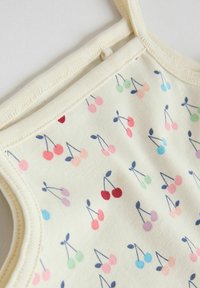 Grenouillère pour bébé couleur crème avec motifs de cerises multicolores et bordure côtelée beige autour du cou et des emmanchures.