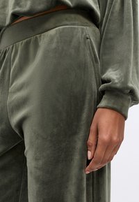 Olijfgroene velours joggers hebben een gladde textuur, een elastische tailleband en zijzakken, met een ontspannen pasvorm en minimale ontwerpelementen.