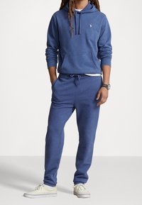 Felpa con cappuccio blu in cotone con tasca a marsupio e cappuccio con coulisse, abbinata a pantaloni della tuta coordinati con vita e polsini elasticizzati.