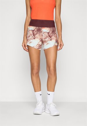 Shorts with a maroon waistband, featuring a multicolored abstract pattern in browns and light blue. Worn with a bright orange top and white sneakers.