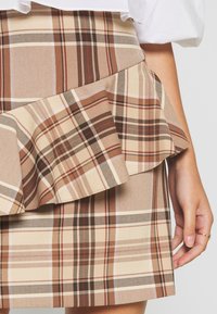 Brąskowa spódnica w kratę z warstwowymi falbanami, z beżowymi, jasnobrązowymi i czerwonymi akcentami. Teksturowany materiał z wyrazistymi wzorami w kratkę.