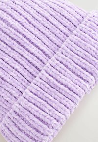 Lila stickad mössa av mjukt, plyschmaterial. Har ribbad textur med växlande upphöjda linjer för ökad detaljrikedom.