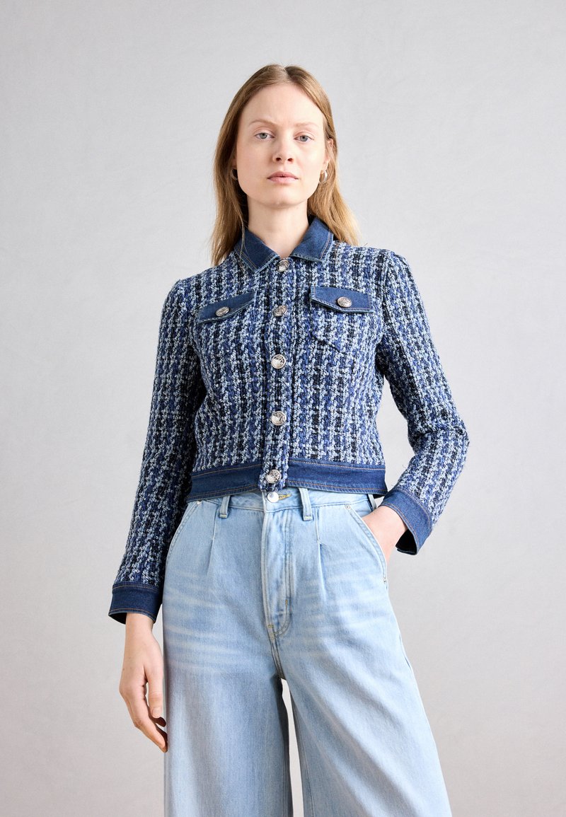 Veste en tweed bleu et blanc avec des accents en denim, dotée d'un col, d'une fermeture à boutons et de poches poitrine. Portée avec un jean large bleu clair.