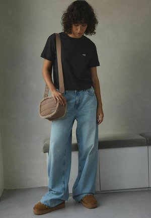 Czarna bawełniana koszulka z małym białym logo, jasno-niebieskie szerokie dżinsy, brązowa torba na ramię z teksturowanej tkaniny oraz brązowe buty na platformie.