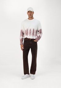 Sudadera de forro polar con tie-dye en blanco y rosa, de cuello redondo, combinada con jeans de pierna recta de color marrón oscuro y zapatillas blancas.