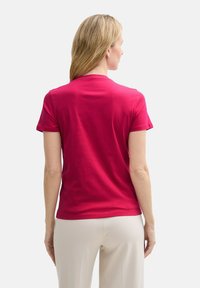 T-shirt ajusté à manches courtes en coton rose vif, avec un col rond et une texture lisse. Porté avec un pantalon de couleur crème.