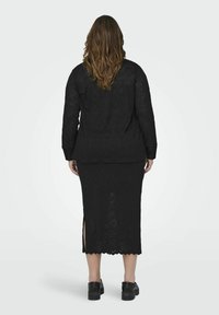 Ensemble deux pièces en dentelle noire comprenant une jupe midi avec des fentes latérales et un haut à manches longues. Le tissu présente un motif floral.