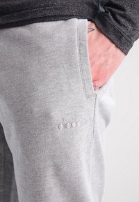 Gray sweatpants made of soft fabric with a side pocket and embroidered branding. Features an elastic waistband and a relaxed fit.