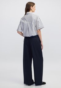 Camicetta a righe bianche e navy a maniche corte abbinata a pantaloni larghi navy. La camicia presenta un colletto e una vestibilità comoda.