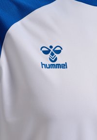 Hvid atletisk skjorte med blå accenter, der har en åndbar tekstur og Hummel-logo i blå på brystområdet.