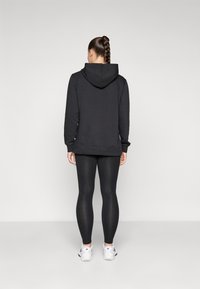 Svart hoodie med dragsko i huvan, långa ärmar och en avslappnad passform, kombinerad med svarta leggings och vita träningsskor.