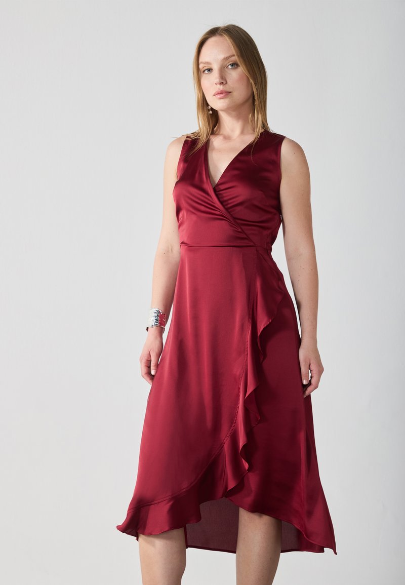 Burgundyröd satinklänning med v-ringning, ärmlös design och asymmetrisk nederkant, med en volangdetalj längs kjolen.
