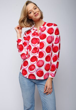Langärmlige Bluse mit weißem Hintergrund und großen roten und rosa Kreis-Mustern. Mit einem geknöpften Ausschnitt und geknöpften Ärmeln.