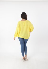 Maglione giallo lavorato a maglia con vestibilità ampia e maniche lunghe, abbinato a jeans skinny blu e sandali trasparenti con tacco. Tessuto a trama liscia.