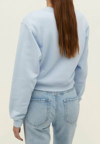Sudadera azul claro con cuello redondo, mangas largas y puños de canalé, combinada con jeans de mezclilla clara de cintura alta que cuentan con bolsillos traseros.