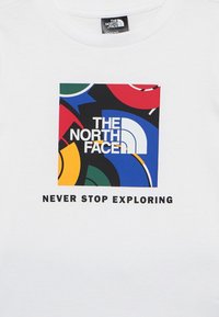 Λευκό πουκάμισο με πολύχρωμο τετράγωνο λογότυπο που φέρει το κείμενο "The North Face" και τη  φράση "Ποτέ μην σταματάς να εξερευνάς" από κάτω.