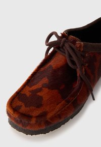 Scarpa con rivestimento in pelliccia marrone, con superficie testurizzata, caratterizzata da un lacci marrone scuro e un design della punta morbida e arrotondata. Suola in gomma.