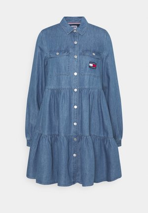 Blauwe denim jurk met lange mouwen, knopen aan de voorkant, twee borstzakken, een geplooide taille en een Tommy Jeans logo patch op de linkerborstzak.