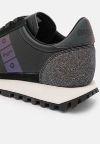 Baskets noires avec talon gris texturé, semelle blanche, bande violette avec des cercles noirs, et logo "Blauer USA" sur le côté et le talon.