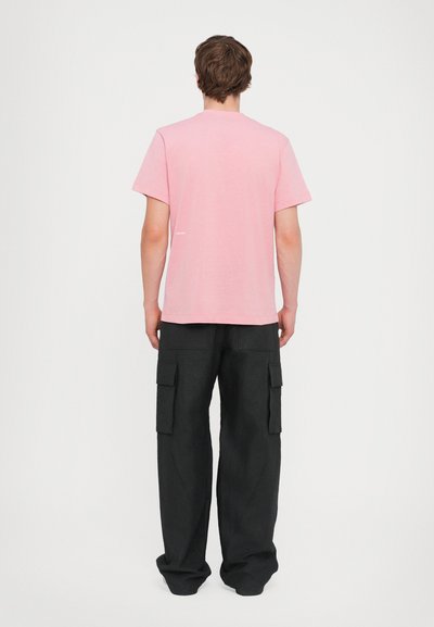 T-shirt rose en coton à col rond, associé à un pantalon cargo noir ample avec plusieurs poches latérales et une finition texturée.