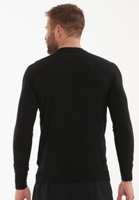 Schwarzes Langarmshirt aus leichtem Stoff, taillierte Passform, Rundhals-Ausschnitt und glatte Textur. Keine sichtbaren Logos oder Muster.