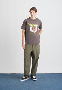 Camiseta de algodón gris con estampado gráfico, combinada con pantalones holgados de color verde oliva y zapatillas negras con cordones blancos. Diseño simple, ajuste casual.